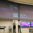 Two students presenting in front of two giant screens