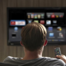 Back of someone's head as they hold a remote and look at a smart TV mounted to the wall
